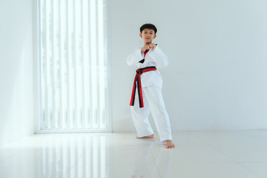 Young boy practices martial arts in a white outfit with a red and black belt in a bright indoor space during daytime