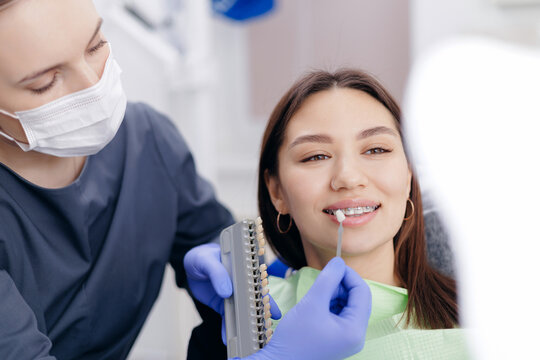 Young female at dentist with tooth shade guide for color matching, choosing dental veneer
