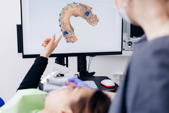 Dentist discussing digital dental 3D scan mold with female patient with braces in dental office