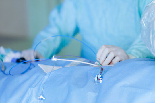 Cardiac catheterization instruments and tubing on sterile blue drape with surgeon hands preparing access for hospital surgery