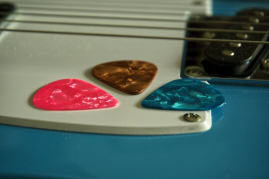 Three plastic guitar plectrums in pink, brown, and blue colors resting on a light blue electric guitar