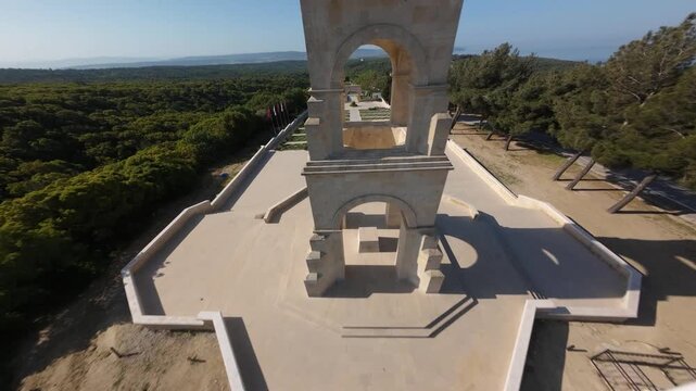 FPV aerial view of the historic Canakkale Martyrs Monument surrounded by dense pine forests and coastal roads in Seddulbahir, Canakkale, Turkiye.