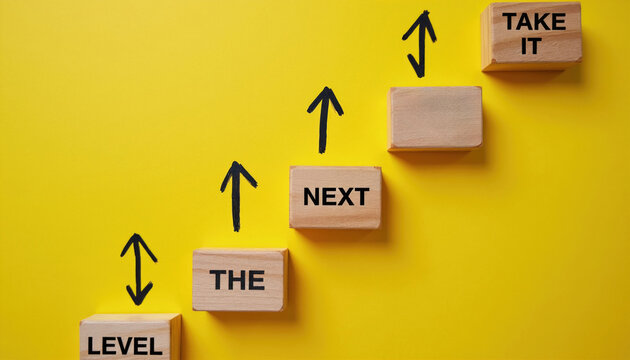 Wooden blocks with text and arrows form stpic. They show concept of moving up to the next level. Phrase take it to the next level is formed visually.