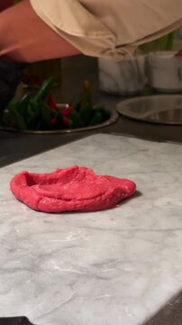 Close-up of a chef seasoning kibbeh nayyeh with ingredients