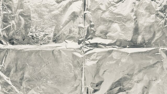 crumpled silver aluminum foil background texture shows metallic crinkled surface reflecting soft industrial ambient light