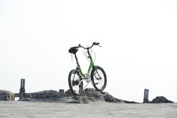 Fototapeta premium Green folding bicycle parked on a rocky surface against a bright.