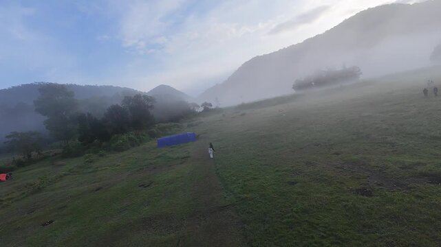 FPV aerial view of the misty Ranca Upas Ciwidey campsite with tents and people surrounded by fog and mountains in Kecamatan Rancabali, Jawa Barat, Indonesia.