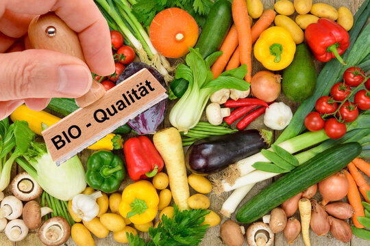 Ein Holzstempel ist beschriftet mit dem Aufdruck: Bio-Qualit&auml;t &uuml;ber frischem Obst und Gem&uuml;se - FOTOMONTAGE
