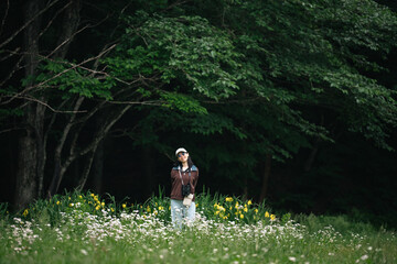 Obraz premium Woman meadow forest flower grass nature outdoor summer green white, woman standing in wildflower meadow near dark forest edge with calm expression, surrounded by green grass and yellow flower