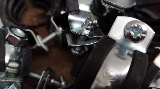 Pile of metal pipe clamps with rubber lining and screws, plumbing hardware close-up
