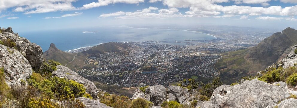 High resolution stitched panorama from Table Mountain, South Africa, showcasing a wide angle view of Cape Town City Bowl, the commercial harbor, Robben Island, and the majestic Devil's Peak summit.