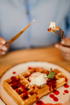 Person eating waffle with whipped cream and raspberry jam