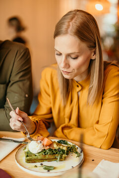 Woman enjoying healthy brunch with green waffles and poached egg