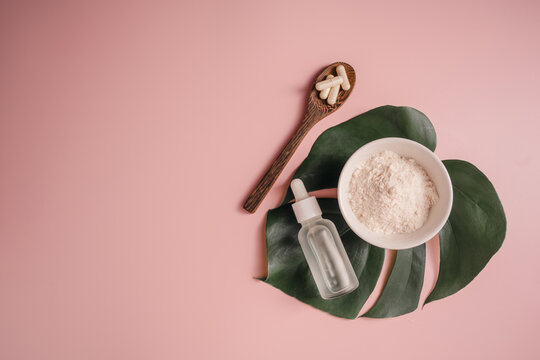 Collagen powder, food supplements capsules and serum bottle on monstera leaf over pink background