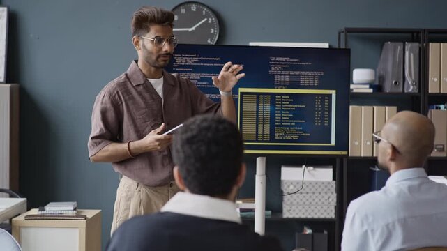 Handheld shot of young Indian man presenting code on screen to multiethnic colleagues in IT office. Footage is suitable for software development training and tech startup marketing