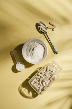 Collagen powder and dietary supplement capsules on yellow background, flat lay