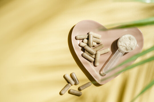 Collagen powder and supplement capsules in heart shaped dish on yellow background, wellness concept