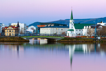Fototapeta premium Twilight view across Tjörnin pond in Reykjavík Iceland with Fríkirkjan church calm reflections and colorful evening sky over the city