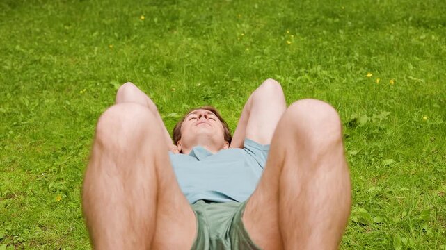 Fit man doing sit-ups on green grass in a summer park. Outdoor workout, fitness, and core exercise for a healthy lifestyle and strong abs. High quality 4k footage