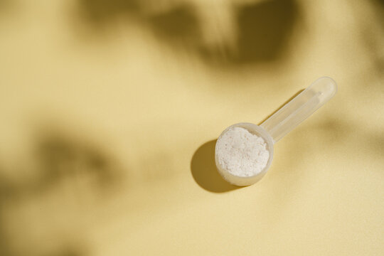 Collagen powder scoop on yellow background with sun light and dark shadows, food supplement concept