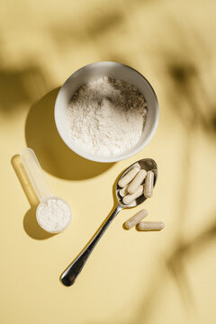 Collagen powder, capsules and scoop on yellow background with sun light and dark shadows, food supplement concept
