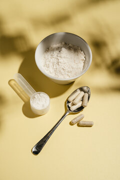Collagen powder, capsules and scoop on yellow background with sun light and dark shadows, food supplement concept