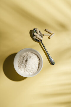 Collagen powder, capsules and scoop on yellow background with sun light and dark shadows, food supplement concept