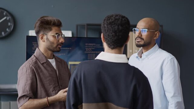 Medium shot of Indian young male IT professionals discussing software development in front of screen with code. Video suits corporate technology presentations and software marketing campaigns
