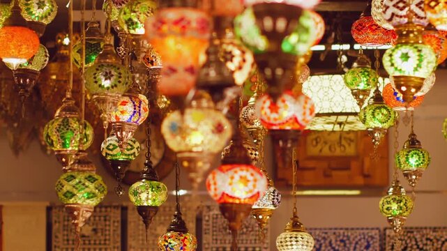 Decorative hanging lanterns with intricate stained glass designs in red, green, orange, illuminated with warm light in traditional Middle Eastern bazaar setting.