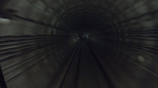 Subway train moving fast at dark tunnel. Speed underground train riding in tunnel. Urban metro driving belowground. Point of view from the railway cabin. Transportation of people concept. Time lapse
