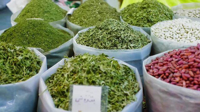 Assorted dried herbs, powdered spices, white seeds, red beans arranged in white containers at outdoor market, showcasing bulk food ingredients, traditional marketplace commerce.