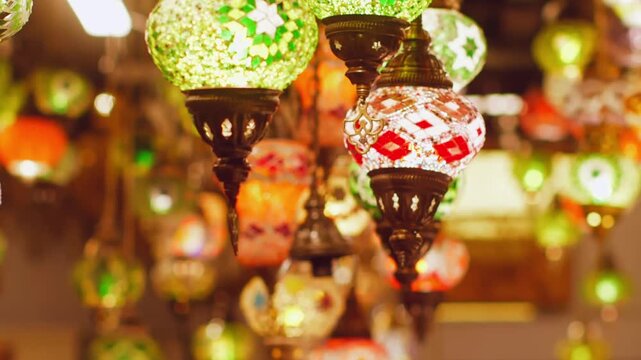Collection of decorative hanging lanterns featuring intricate colored glass mosaics in green, red, orange, brass fixtures creating warm ambient lighting in traditional bazaar setting.