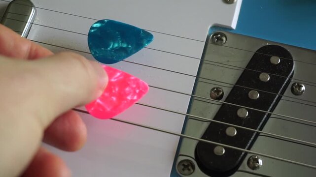 Musician's hand placing multiple colorful plectrums between the strings of a blue electric guitar