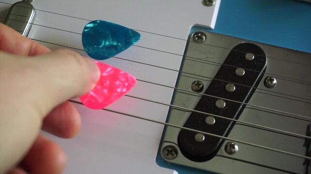 Close-up of a hand placing various colorful guitar picks between the strings of an electric guitar