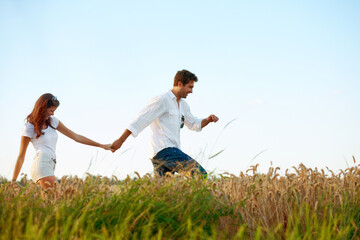 Obraz premium Couple, holding hands and walking in meadow with blue sky, partner and support with care in nature. People, marriage and romantic stroll for healthy relationship, bonding together and space for love