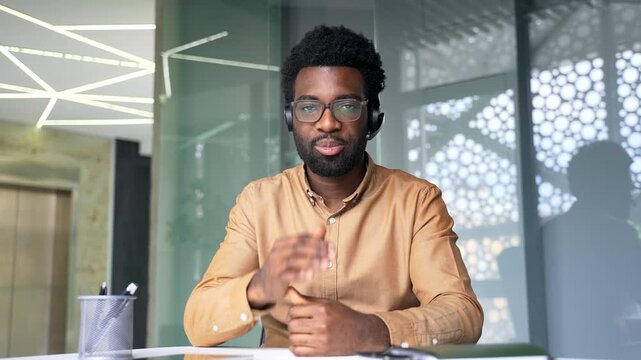 Webcam view of confident African American coach wearing headset looking at camera during online training. Black man instructor speaking and conducting virtual seminar or webinar from office workplace.