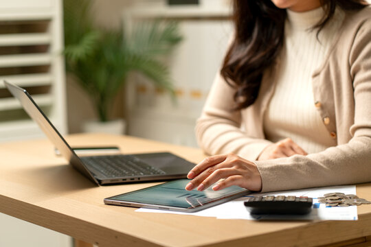 Front view close up left hand of woman touch and work with tablet near calculator, laptop and coins on table in concept of new technology to support the success of business.