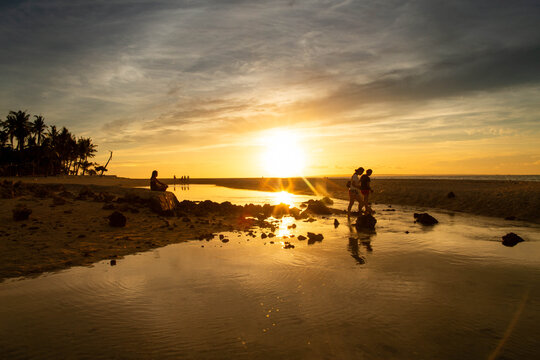 Cebu, Philippines - 21 June 2026: View of Bantayan Island at sunset with people walking along the shallow shoreline and palm trees silhouetted against the golden sky.