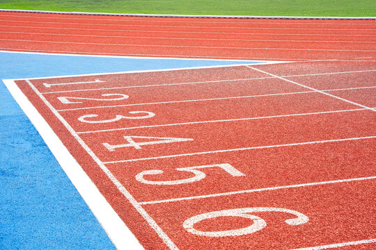 Red running track starting line with white lane numbers 1 to 6 and blue surface. High angle view of empty athletic stadium race track. Ideas for sports and business concept.