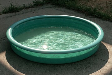 Fototapeta premium Teal Inflatable Pool on Cracked Concrete, Sunlight Reflecting Off Water Surface