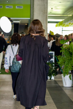 graduate girl in black robe standing indoors, traditional, academic, campus, among graduates, graduation, confederate