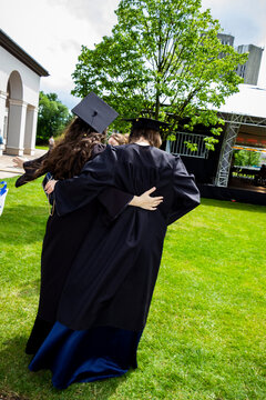 blond graduate girl and a guy in a scarf-style traditional academic black robe are walking in a student campus, among graduates, graduation, confederate