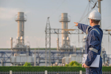 Fototapeta premium Asian male electrical engineer holding digital tablet standing at power plant station. Professional energy industry technician working on infrastructure maintenance and renewable resource project.