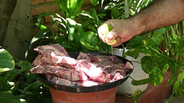 Agregando jugo de lim&oacute;n a cortes de carne vacuna para preparar un asado argentino al aire libre