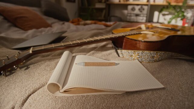 Acoustic guitar, open notebook with pen, and laptop resting on bed in home studio. Clip is perfect for promoting music education, songwriting courses, or creative lifestyle brands