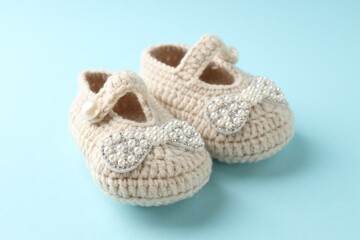 Cute knitted baby shoes on light blue background, closeup