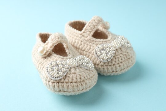 Cute knitted baby shoes on light blue background, closeup