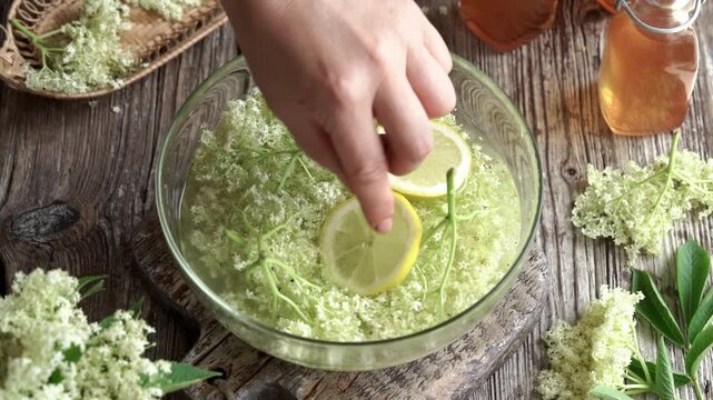 Adding lemon into a bottle with fresh elderberry flowers - preparation of homemade herbal syrup