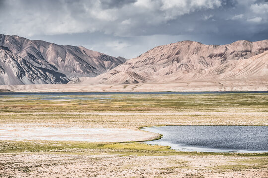 Landscape in the Pamir Mountains in valley with green grassy meadows and pastures, mountain range rises in the Tien Shan Mountains, panoramic landscape for background