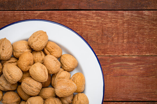 English walnuts nuts on white metal enamel plate against rustic wood, top view with a copy space